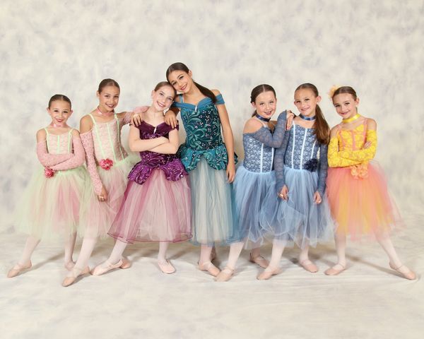 Seven young ballerinas in colorful tutus posing together.