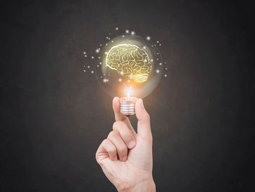 Hand holding a glowing light bulb with a brain illustration inside.
