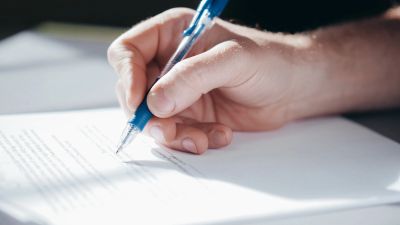 Hand signing a document with a blue pen.