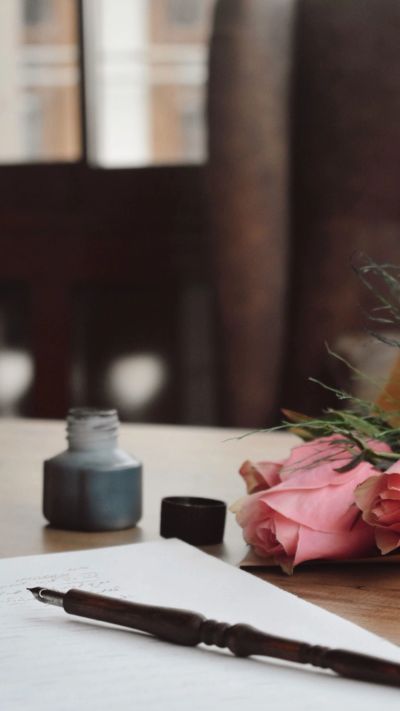 Ink bottle, rose, and pen on paper on a wooden table.