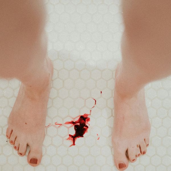 clot of blood on a white tile floor between feet