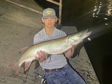 Young man holding a large fish by the water at night.