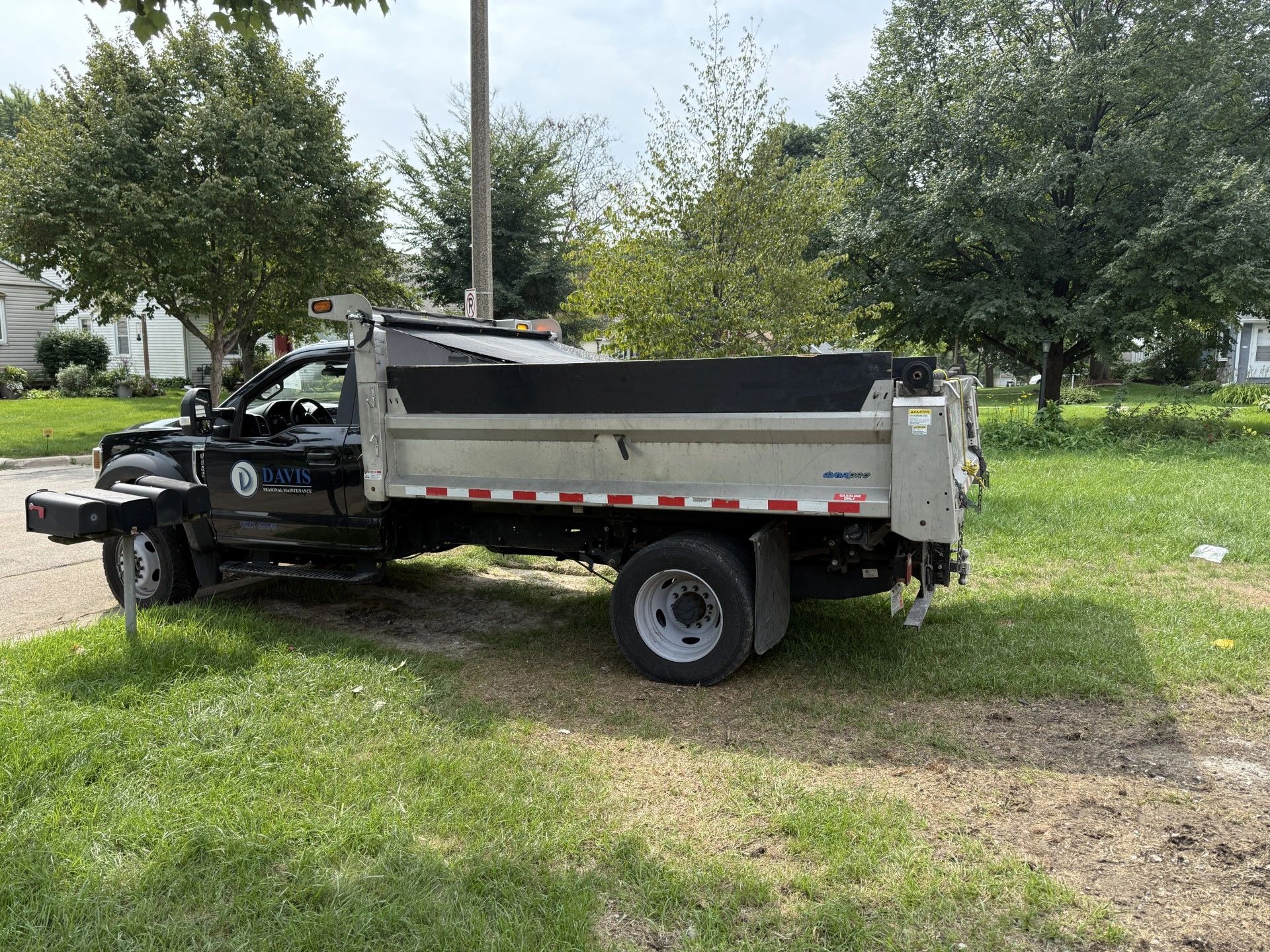 Black dump truck parked on grass near trees in a residential area.