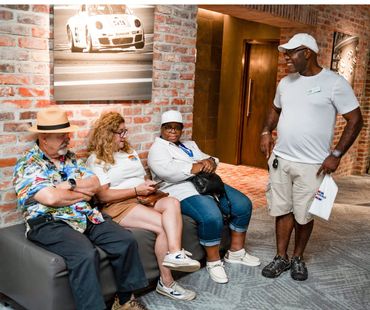 Four adults casually chatting in a cozy brick-walled room with racing photos.