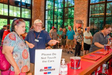 People gather indoors at a Brumos event with a sign asking not to touch the cars.
