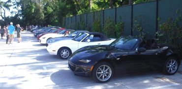 A lineup of Mazda MX-5 Miata cars parked outdoors with people nearby.