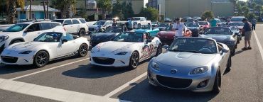 A gathering of Mazda MX-5 Miata convertibles lined up in a parking lot on a sunny day.