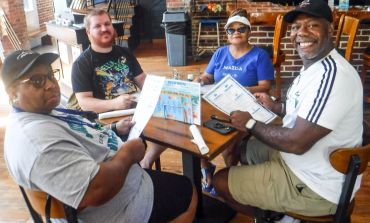 Four people sitting at a restaurant table holding menus and smiling.