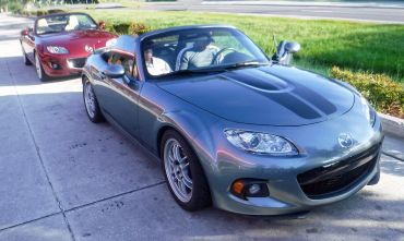 Two Mazda MX-5 Miata convertibles parked on a sunny street.