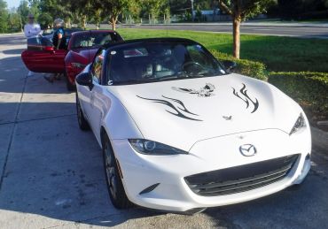 White Mazda convertible with black decals parked on the side of the street.