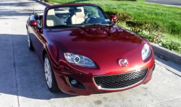 A shiny red Mazda convertible parked on a driveway.