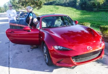 Red Mazda sports car with its door open and people nearby.