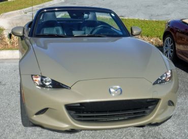 Front view of a beige Mazda convertible parked outdoors.