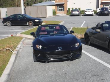 Black Mazda convertible parked in a lot with red interior seats.