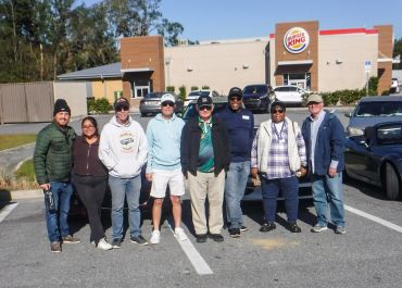 A group of eight people standing in a parking lot in front of a Burger King.