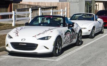 Two white Mazda Miata convertibles parked in a row on the street.