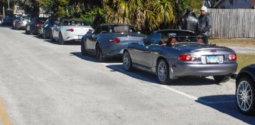 A lineup of convertible sports cars parked along a street on a sunny day.