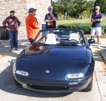 Classic Mazda Miata convertible with four men standing nearby.