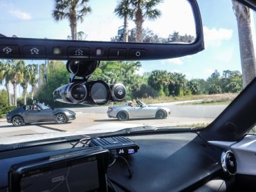Two convertible sports cars on a sunny road, seen from inside another car.