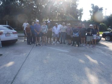 A group of people standing outdoors in a parking lot on a sunny day.