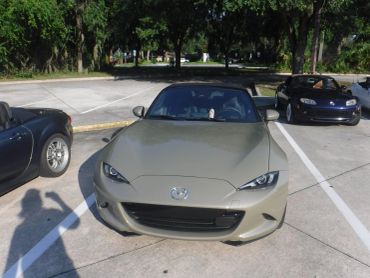 Front view of a beige Mazda MX-5 Miata convertible in a parking lot.