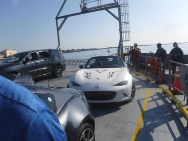 Cars and people on a ferry boat with water in the background.