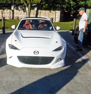 White Mazda sports car parked with a man smoking a cigar nearby.