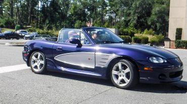 Purple convertible sports car with silver side panels on a sunny day.