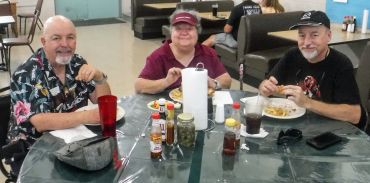 Three people enjoying a meal together at a round table with condiments.