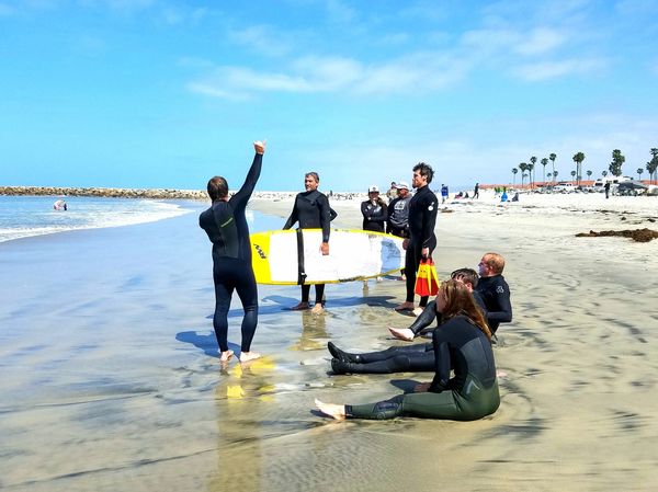 Group of volunteers and a surfer having a pre surf pow wow in sand on the tide line.