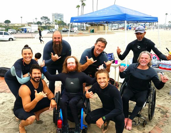 Image of volunteers with surfers Mike and Albert throwing up shakas on the beach.