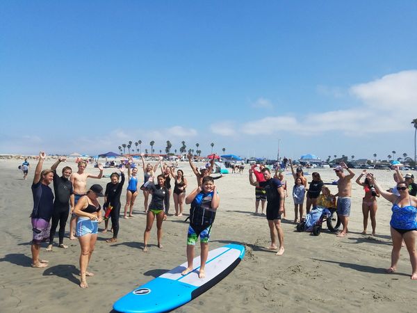 Large group of surfers and volunteers throwing up shakas on a beautiful summer day.