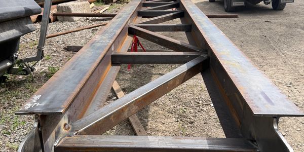 Steel beams with diagonal braces arranged on the ground outdoors.