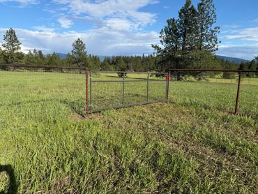 A metal gate in a fenced grassy field under a partly cloudy sky.