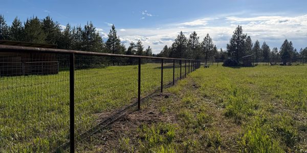 A wire fence runs through a green field under a partly cloudy sky.