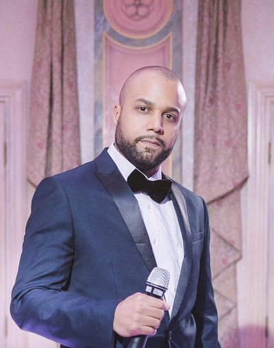 Man in tuxedo holding a microphone, ready to speak or perform.