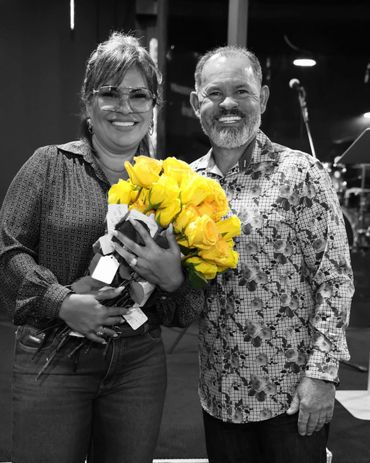 A smiling couple poses with a vibrant bouquet of yellow roses in black-and-white surroundings.