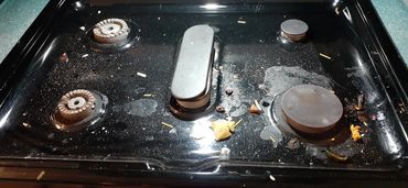 A dirty black stovetop with food crumbs and stains.