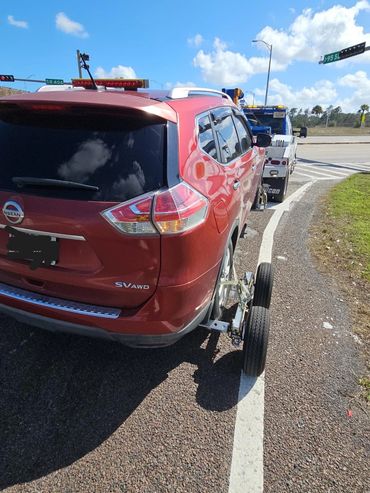 Red Nissan SUV being towed on a roadside under a clear sky.