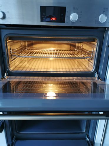 Open modern oven with light on and digital clock displaying 12:09.