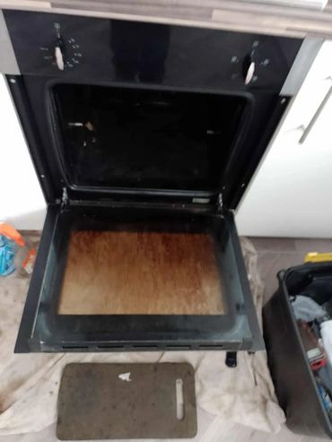 Open oven with a dirty baking tray removed and placed on cloth.