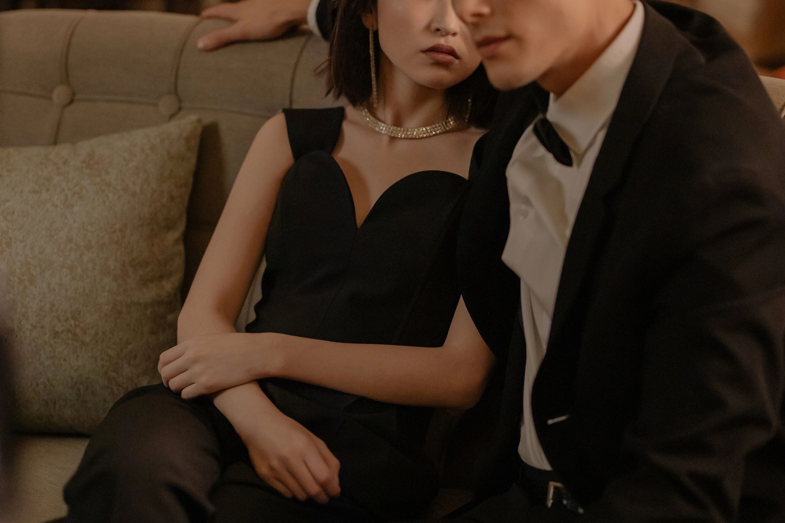 Elegant couple dressed in black formal wear sitting closely on a sofa.