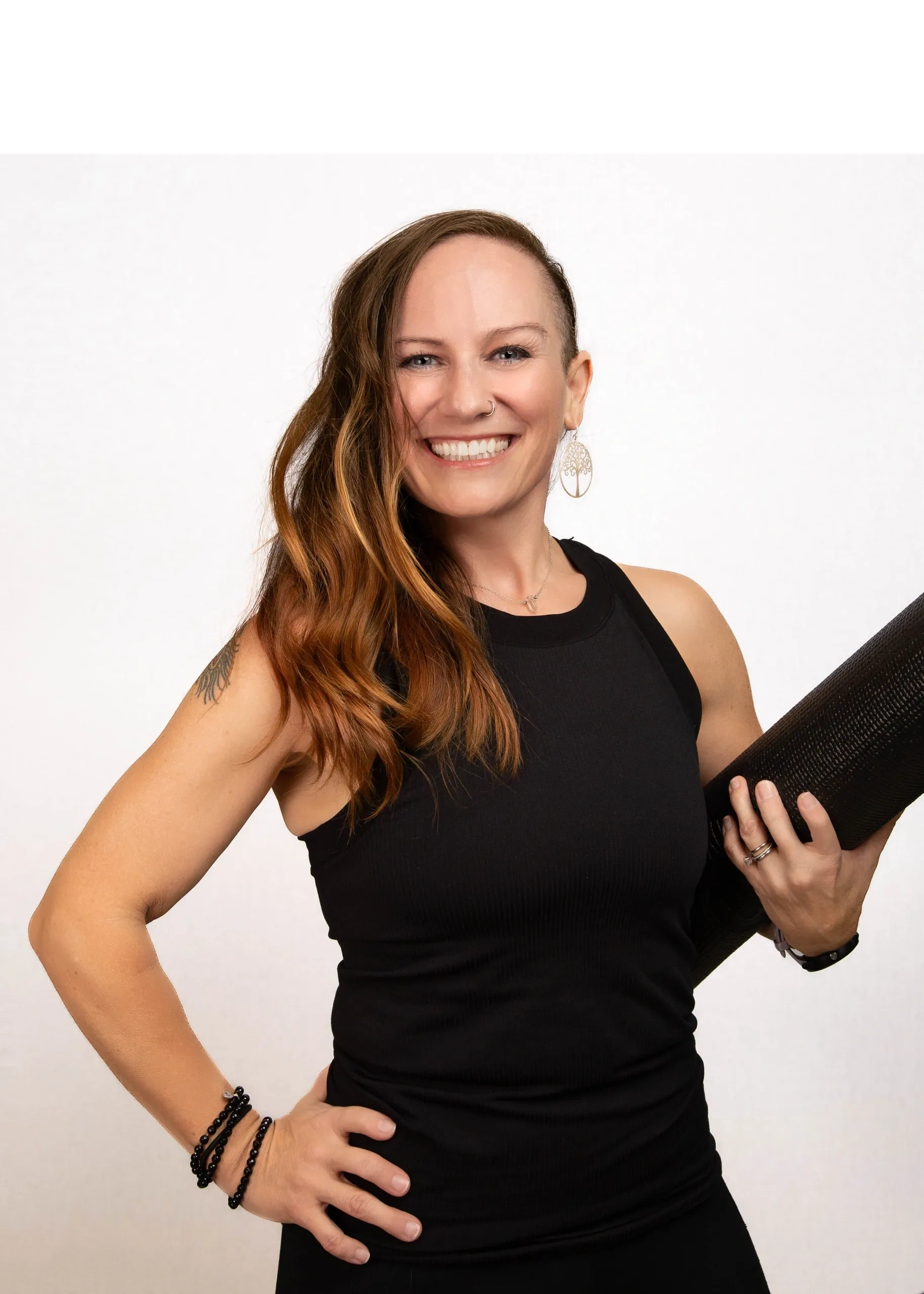 A smiling woman dressed in black athletic clothes holding a yoga mat