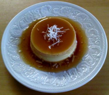 Caramel flan dessert topped with shredded coconut on a decorative plate.