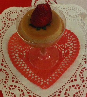 Flan dessert topped with a fresh strawberry on a heart-shaped doily.