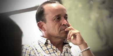 A man in a checkered shirt thoughtfully resting his hand on his chin.
