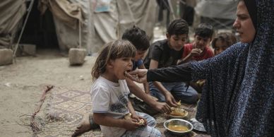 A woman feeding a child in a refugee camp with other children around.