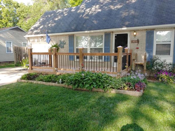 Cozy house with a wooden porch and a lush garden in front.