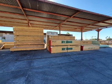 Stacks of lumber under a metal roof in a lumber yard.