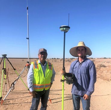 Two men standing in a dry field with surveying equipment.